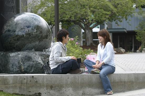 photo of two  students sitting near a water sculpture on campus.