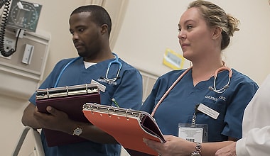 Photo of two  nursing students, one female and one male, holding clipboards during a class session.