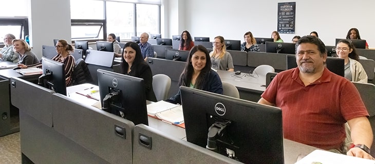 Adult  students sitting in front of computers in a classroom.